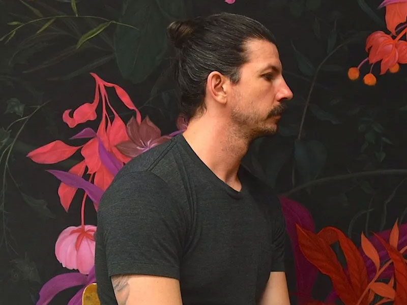 Artist Zachari Logan in profile in front of a mural of pink flowers and green leaves