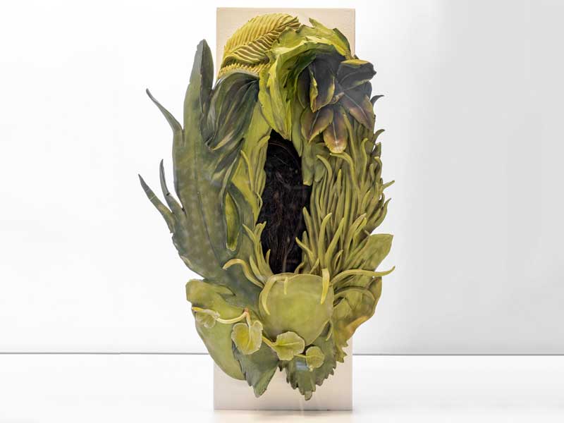 Ceramic sculpture of a green plant form with braided hair at the centre